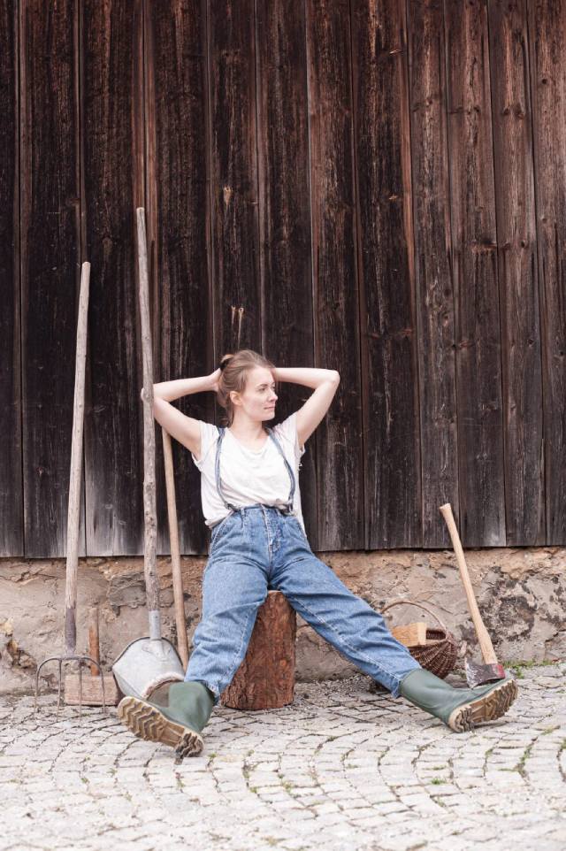 Darstellerin sitzt auf Holzpflock vor einer Scheune