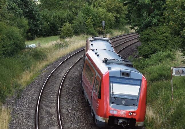 Ein roter Zug fährt auf Schienen in Richtung Speichersdorf